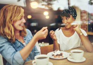 46626158 - two charismatic multi ethnic young girl friends sit at a counter in a cafe enjoying a cup of coffee while laughing and chatting