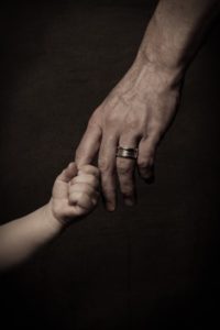 26733572 - child's small hand holding finger of his father, dark key