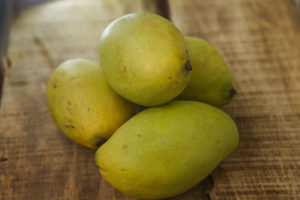 55242674 - closeup picture of four green ripe mangos on ripped brown wooden table background